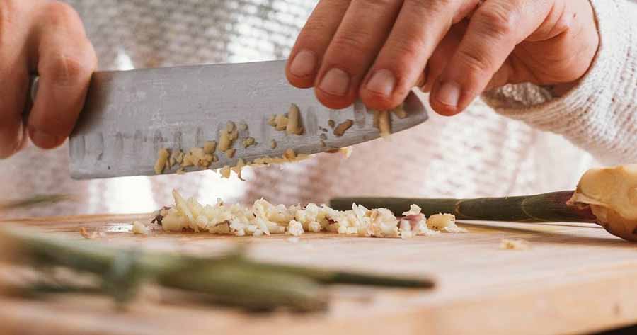 A person holding a knife and slicing vegetables